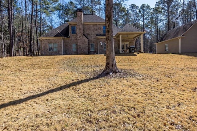 rear view of property featuring brick siding, a lawn, a chimney, and a shingled roof