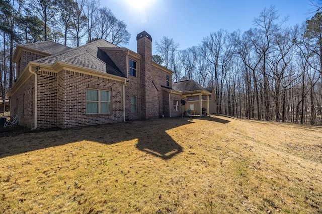 back of house featuring a lawn, brick siding, and a chimney