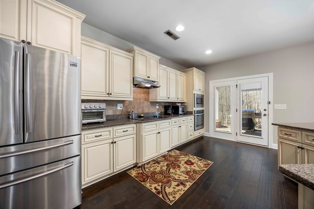 kitchen with under cabinet range hood, cream cabinetry, appliances with stainless steel finishes, and visible vents