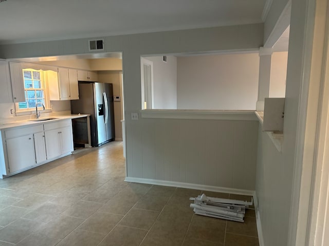 kitchen with wood walls, stainless steel fridge, white cabinets, light tile patterned flooring, and sink