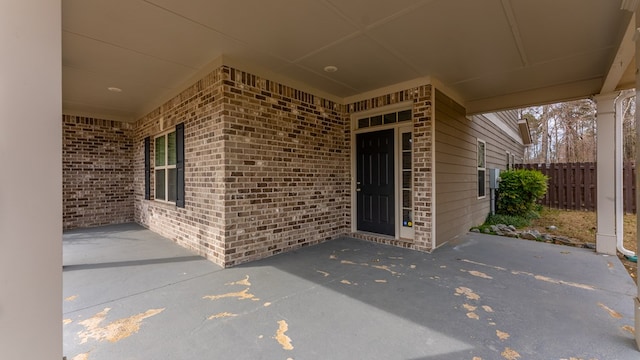 view of exterior entry featuring brick siding, fence, and a patio area