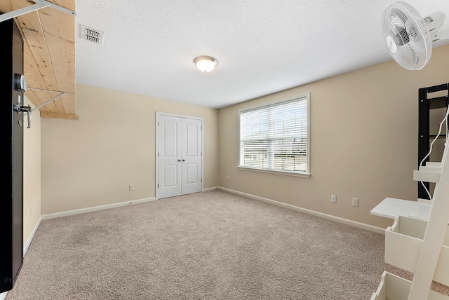 carpeted empty room featuring baseboards, a textured ceiling, and visible vents