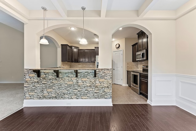 kitchen with beam ceiling, dark brown cabinetry, stainless steel appliances, and pendant lighting