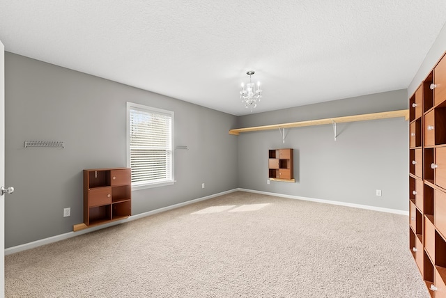 unfurnished room with a notable chandelier, carpet floors, a textured ceiling, and baseboards