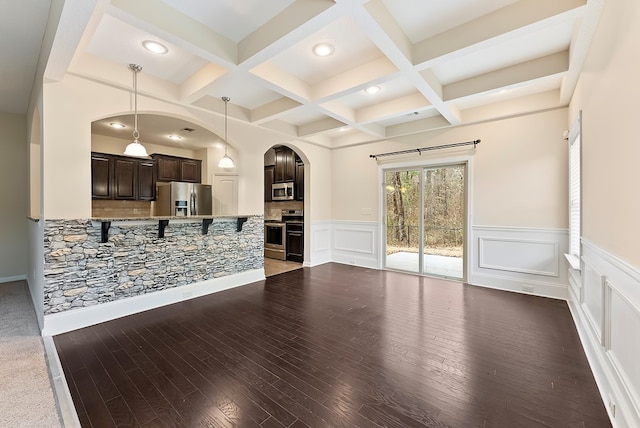 living area with arched walkways, coffered ceiling, and beam ceiling