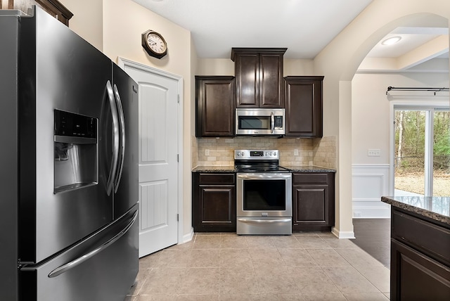 kitchen with dark stone counters, appliances with stainless steel finishes, dark brown cabinets, and decorative backsplash