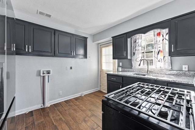 kitchen with black gas stove, a sink, baseboards, light stone counters, and dark wood-style floors