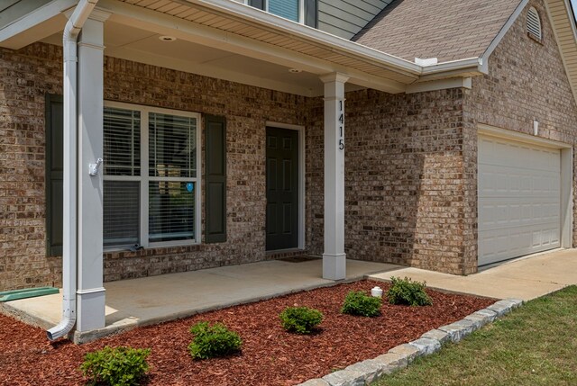 doorway to property with brick siding, a porch, and an attached garage