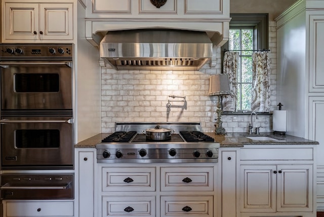 kitchen featuring decorative backsplash, dark stone counters, stainless steel appliances, and wall chimney exhaust hood