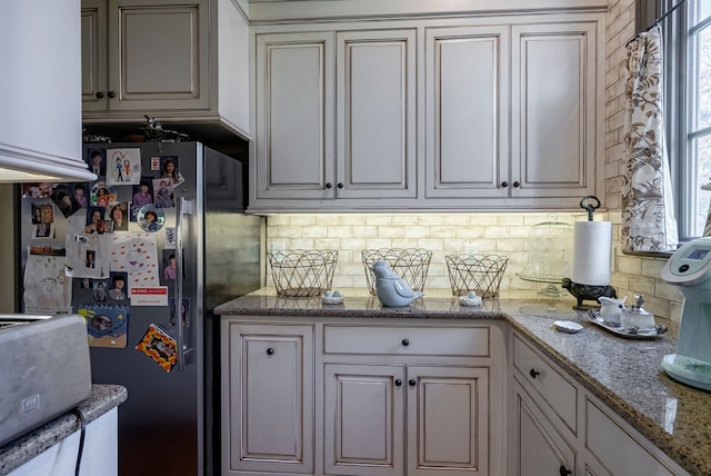 kitchen with white cabinets, stainless steel fridge, light stone countertops, and tasteful backsplash