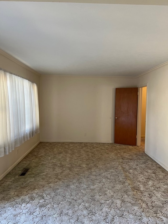 carpeted spare room featuring visible vents, baseboards, and crown molding