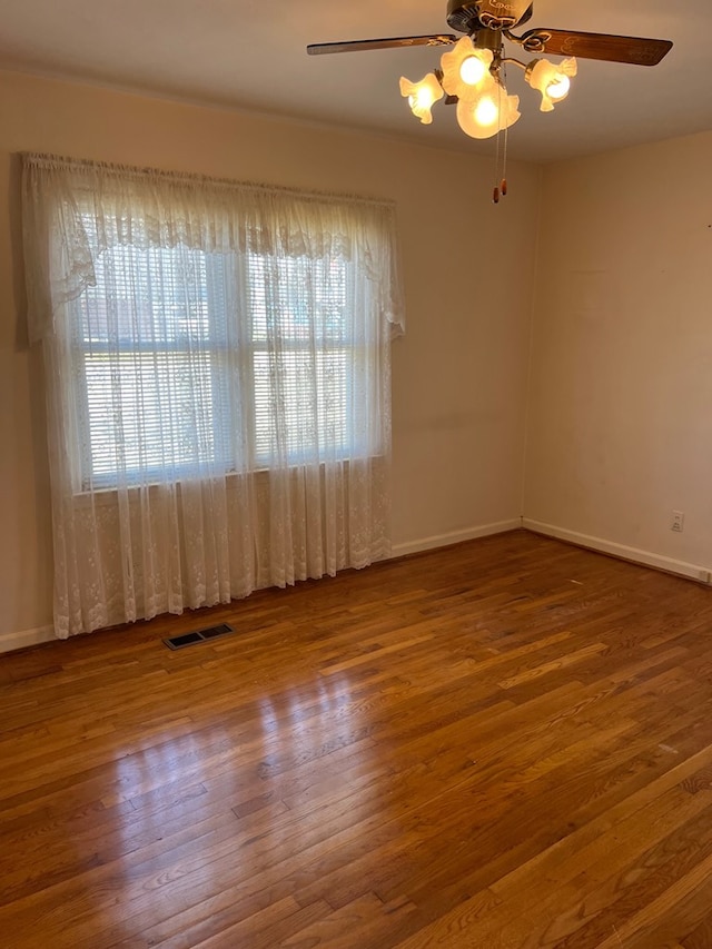 empty room with visible vents, ceiling fan, baseboards, and wood finished floors