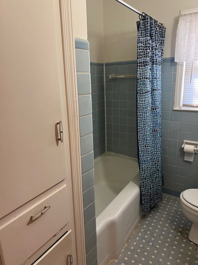 full bath with toilet, shower / bath combo, tile walls, and wainscoting