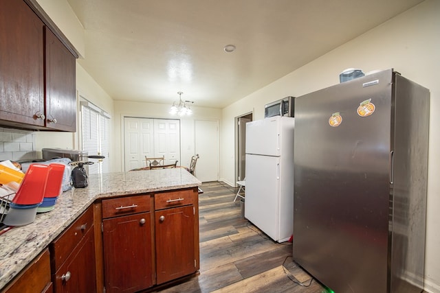 kitchen featuring dark wood-style flooring, stainless steel appliances, backsplash, an inviting chandelier, and a peninsula