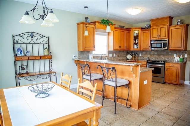 93 Pebble Ct, Smiths Station, AL 36877 - kitchen featuring stainless steel appliances, decorative backsplash, brown cabinetry, a peninsula, and a textured ceiling