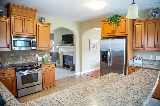 93 Pebble Ct, Smiths Station, AL 36877 - kitchen featuring stainless steel appliances, light tile patterned flooring, light stone counters, brown cabinetry, and a textured ceiling