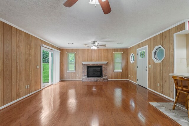 unfurnished living room with crown molding, a ceiling fan, a brick fireplace, and baseboards