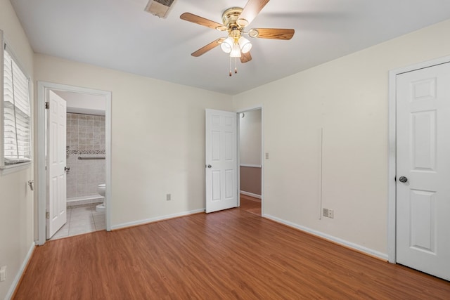 unfurnished bedroom with connected bathroom, visible vents, baseboards, wood finished floors, and a ceiling fan