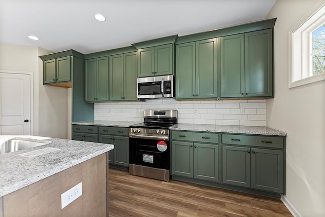 kitchen with green cabinets, light stone countertops, appliances with stainless steel finishes, and tasteful backsplash