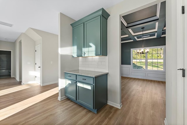 interior space featuring decorative backsplash, light stone counters, coffered ceiling, light hardwood / wood-style flooring, and a notable chandelier