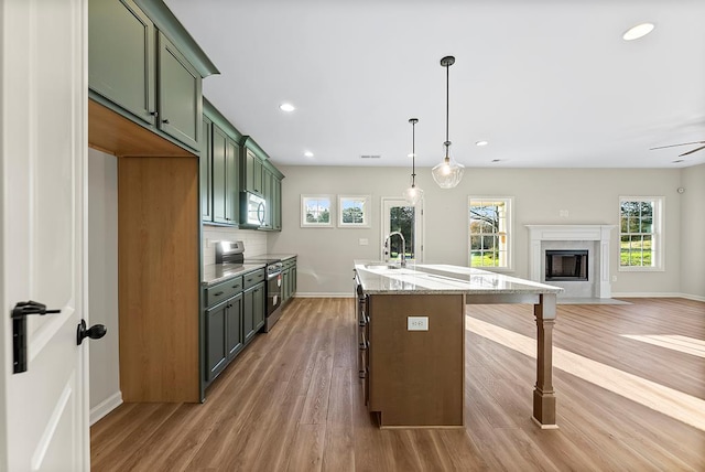 kitchen with pendant lighting, electric stove, green cabinetry, an island with sink, and light stone counters