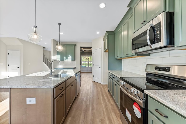 kitchen featuring light stone countertops, hanging light fixtures, green cabinets, a kitchen island with sink, and appliances with stainless steel finishes