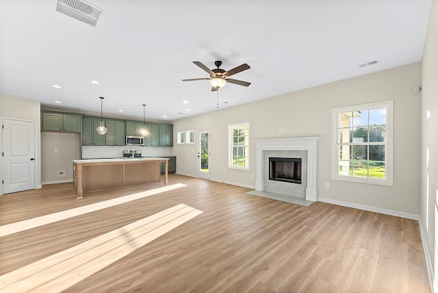 unfurnished living room featuring ceiling fan, light hardwood / wood-style flooring, a high end fireplace, and plenty of natural light