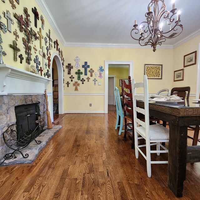 dining space with a stone fireplace, a chandelier, wood-type flooring, and ornamental molding