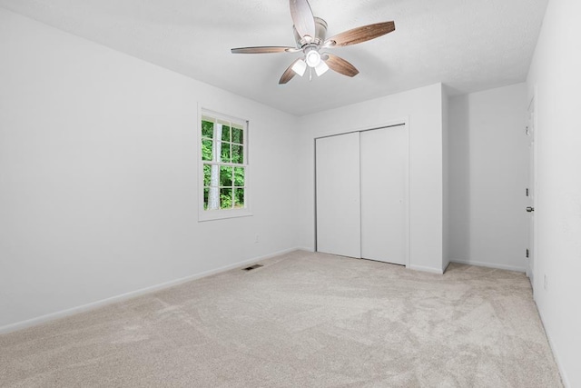 unfurnished bedroom featuring ceiling fan, a closet, and light colored carpet