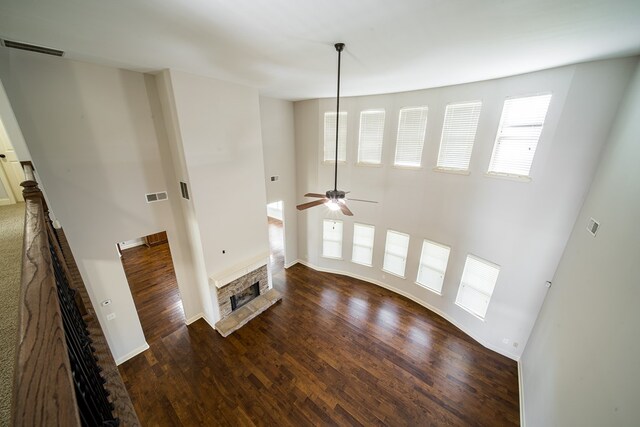 unfurnished living room with dark hardwood / wood-style flooring, ceiling fan, a stone fireplace, and a high ceiling