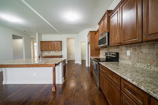 kitchen with light stone countertops, appliances with stainless steel finishes, a kitchen island with sink, sink, and dark hardwood / wood-style floors