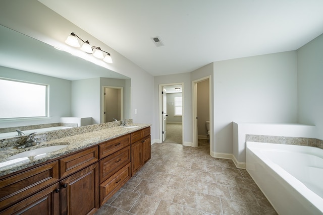 bathroom featuring vanity, a tub to relax in, and toilet