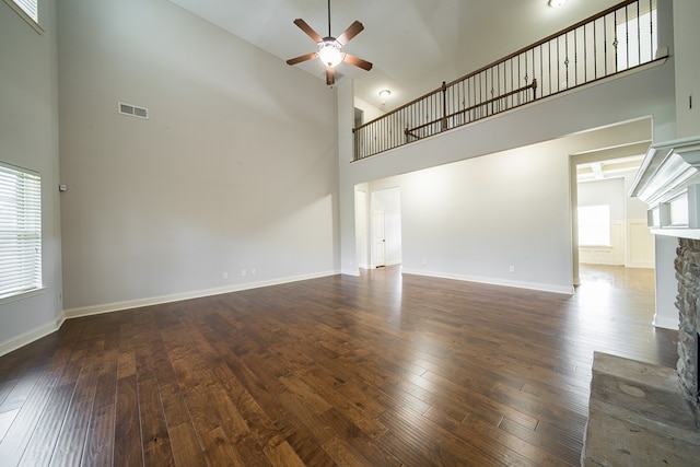 unfurnished living room featuring ceiling fan, a towering ceiling, a fireplace, and dark wood-type flooring