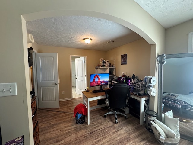 home office with arched walkways, a textured ceiling, and wood finished floors