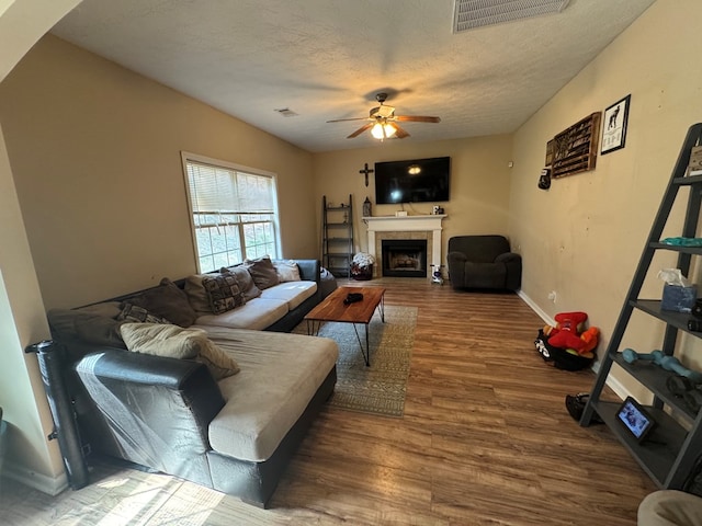 living room featuring visible vents, a fireplace, wood finished floors, a textured ceiling, and a ceiling fan