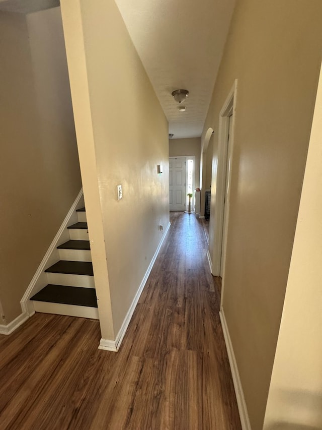 hall featuring stairs, dark wood-type flooring, and baseboards