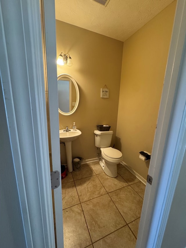 half bathroom with toilet, a sink, a textured ceiling, tile patterned flooring, and baseboards