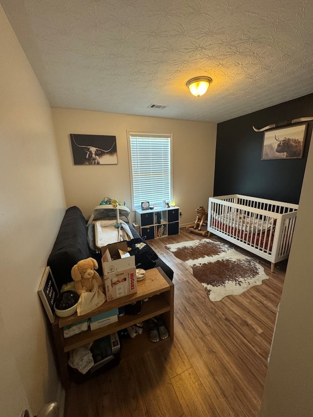 bedroom with visible vents, a textured ceiling, baseboards, and wood finished floors