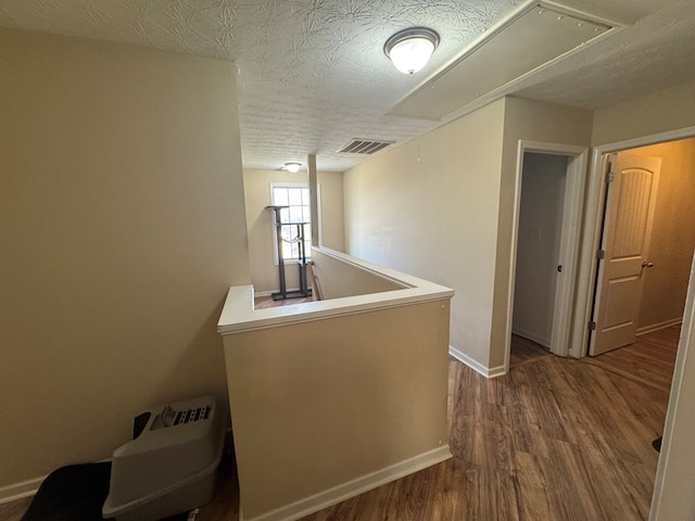 corridor with visible vents, an upstairs landing, a textured ceiling, wood finished floors, and attic access