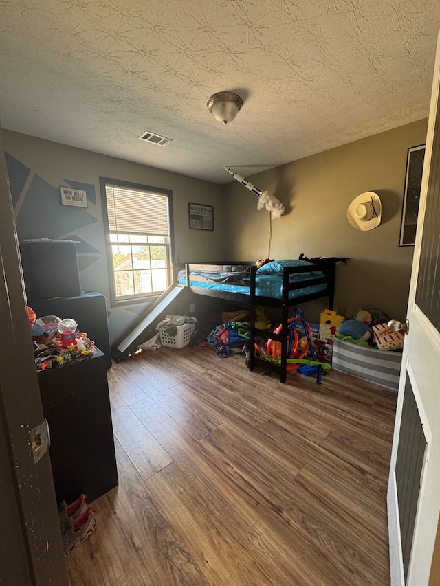 bedroom featuring visible vents, a textured ceiling, and wood finished floors