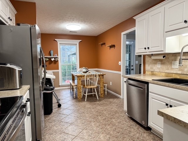 kitchen featuring a sink, backsplash, white cabinetry, appliances with stainless steel finishes, and light countertops