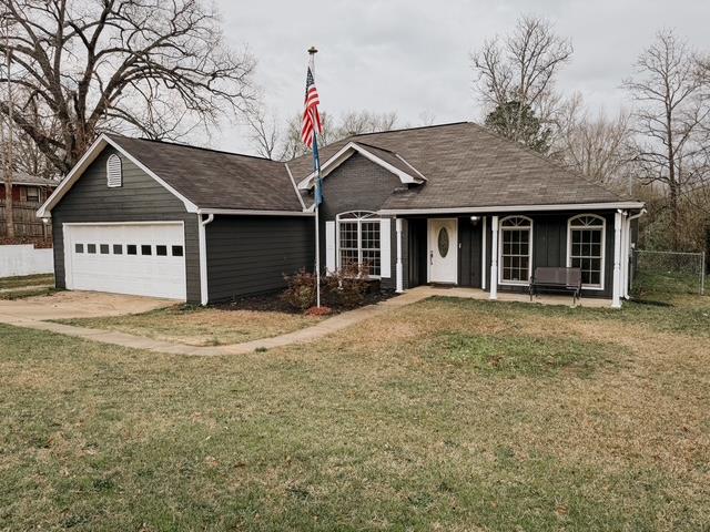 ranch-style home featuring driveway, an attached garage, a front yard, and fence