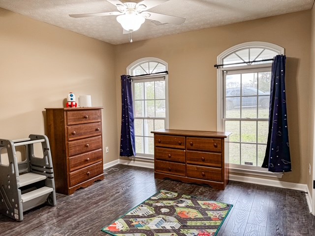 living area with dark wood finished floors, ceiling fan, baseboards, and a textured ceiling