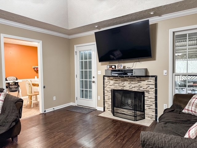 living area with wood finished floors, baseboards, a tile fireplace, a textured ceiling, and crown molding