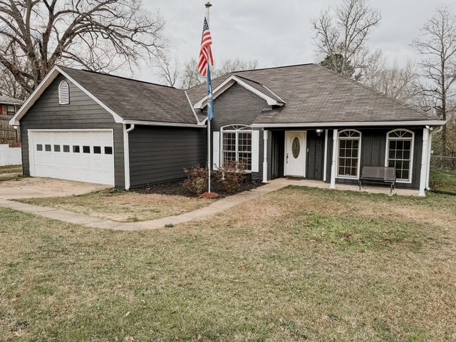 single story home featuring a front lawn, a garage, driveway, and a shingled roof