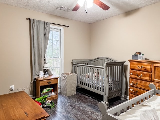 bedroom with ceiling fan, visible vents, a textured ceiling, and wood finished floors