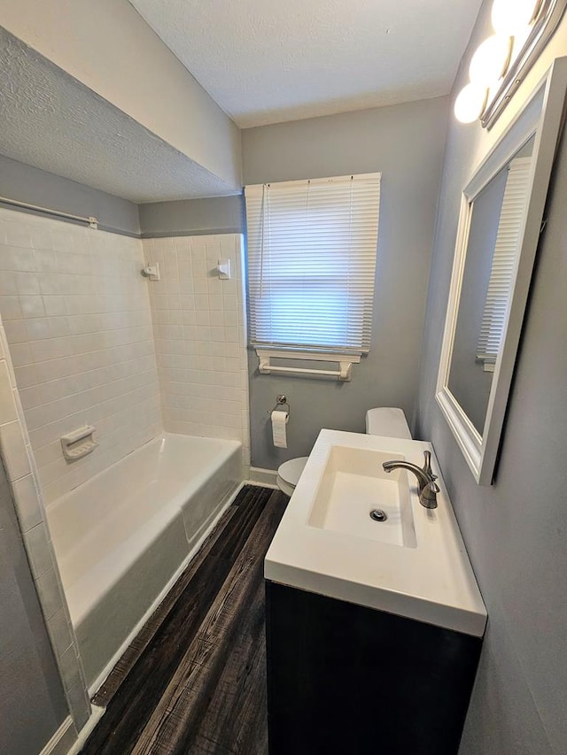 full bathroom with tiled shower / bath combo, hardwood / wood-style floors, a textured ceiling, toilet, and vanity