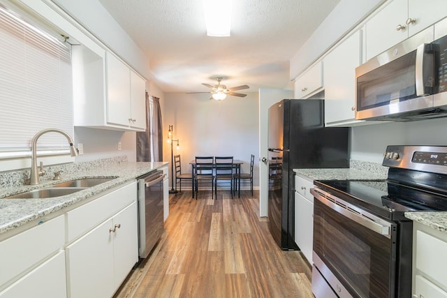 kitchen with appliances with stainless steel finishes, ceiling fan, sink, white cabinets, and hardwood / wood-style floors