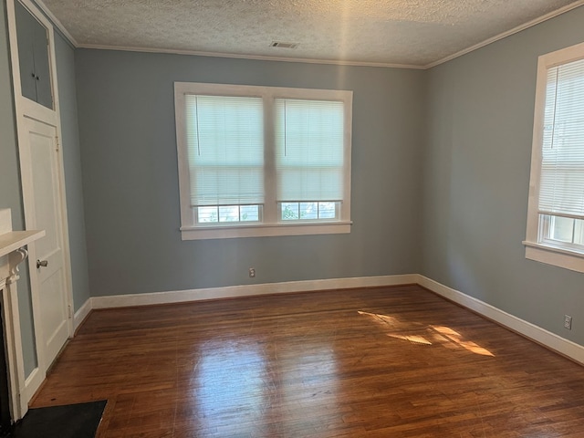 spare room featuring a textured ceiling, dark wood finished floors, baseboards, ornamental molding, and visible vents