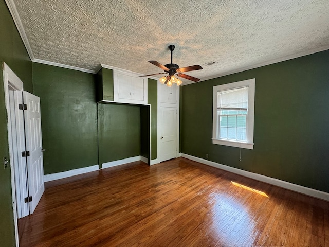 unfurnished bedroom featuring wood finished floors, visible vents, ornamental molding, baseboards, and a textured ceiling